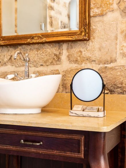 Elegant stone sink with a round mirror in the boutique suite bathroom at Flora Valley Boutique Hotel, Ein Kerem, Jerusalem
