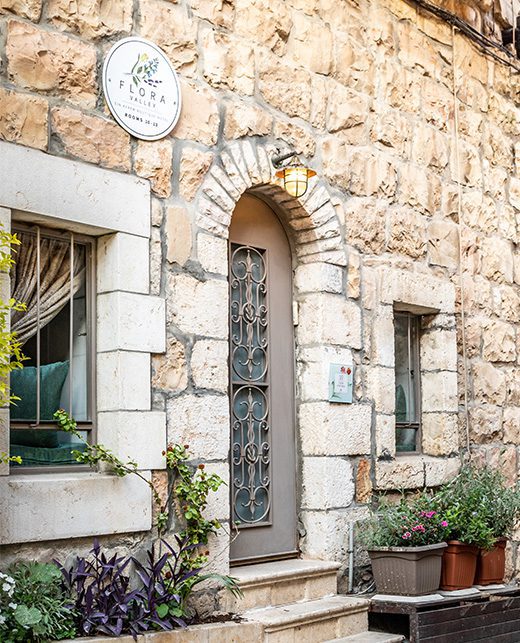 The entrance to Suite 12 at Flora Valley Boutique Hotel in Ein Kerem, Jerusalem – a charming stone doorway surrounded by lush greenery and blooming planters, offering an authentic boutique stay in a pastoral setting