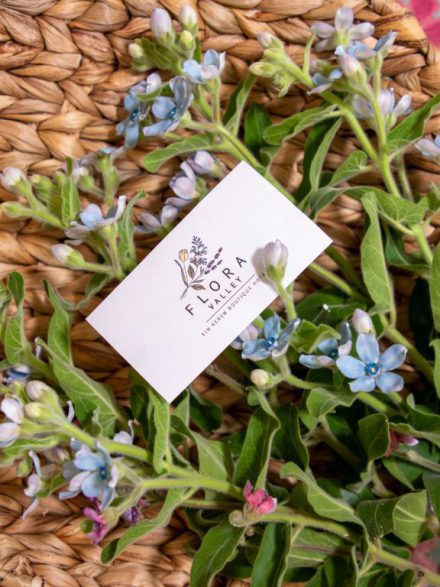 Flora Valley Boutique Hotel business card placed on a bed of flowers and fresh herbs.